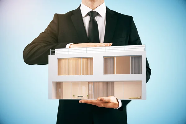 Businessman holding modern house on light blue background. Property concept. 3D Rendering — Stock Photo, Image