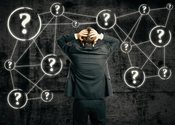 Back view of stressed businessman on concrete background with connected question marks. Confusion concept — Stock Photo, Image