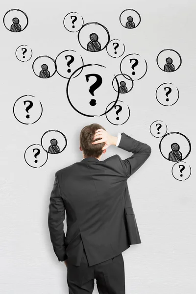 Back view of stressed young businessman on concrete background with question marks and HR icons. Hiring concept — Stock Photo, Image