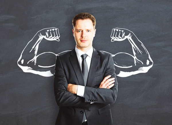 Confident businessman with drawn muscly hands on chalkboard background. Power concept — Stock Photo, Image