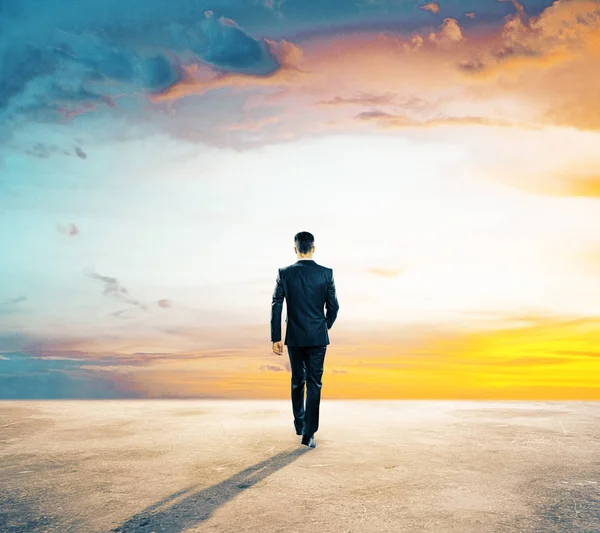 Vista trasera de un joven hombre de negocios caminando sobre suelo de hormigón. Hermoso cielo en el fondo. Concepto de futuro —  Fotos de Stock