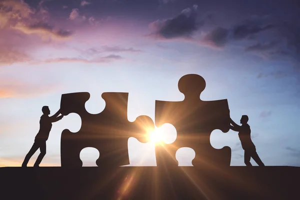 Mensen silhouetten zetten puzzel stukjes samen op de mooie hemelachtergrond met zonlicht. Concept van het partnerschap — Stockfoto