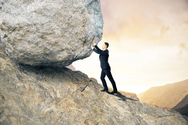 Side view of young businessman pushing huge rock up mountain. Beautiful background. Effort concept — Stock Photo, Image