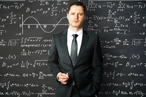 Портрет красивого молодого бизнесмена с мелом в руках. Доска с математическими формулами на заднем плане. Концепция образования — стоковое фото