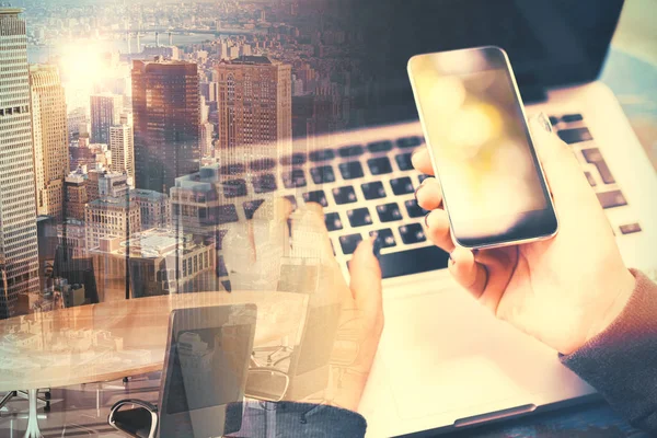Κοντινό πλάνο της αρσενικό χέρια με laptop και smartphone σε αφηρημένη πόλη φόντο. Συσκευές έννοια. Διπλή έκθεση — Φωτογραφία Αρχείου