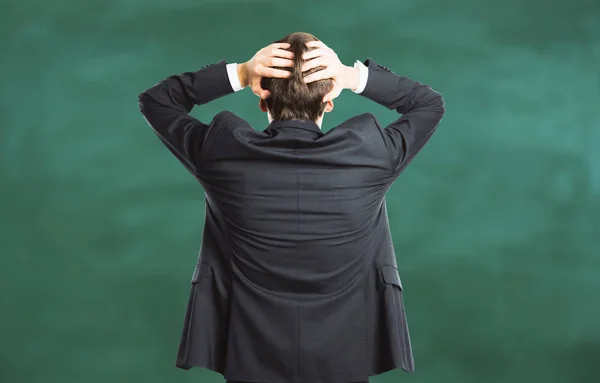 Back view of stressed young businessman on blackboard background. Overworked concept — Stock Photo, Image