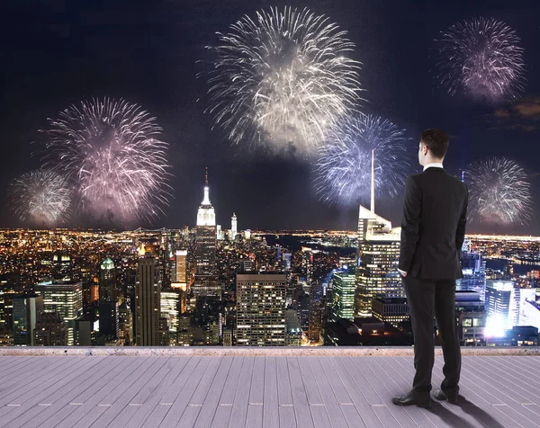 Joven hombre de negocios en el muelle mirando la ciudad nocturna con fuegos artificiales. Concepto de vacaciones — Foto de Stock