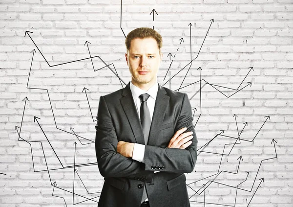 Portrait of confident young businessman with folded arms on white brick background with numerous arrows. Choice concept — Stock Photo, Image