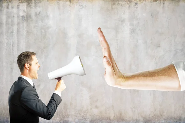 Hand gestures no to businessman screaming into megaphone on concrete background. Communication concept