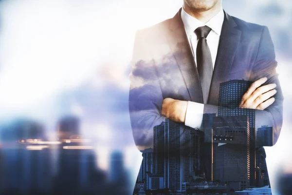 Young businessman with folded arms standing on city background with copy space. — Stock Photo, Image