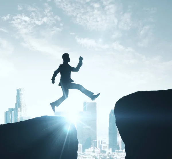 Backlit image of man silhouette jumping off cliff on city background. Success concept — Stock Photo, Image