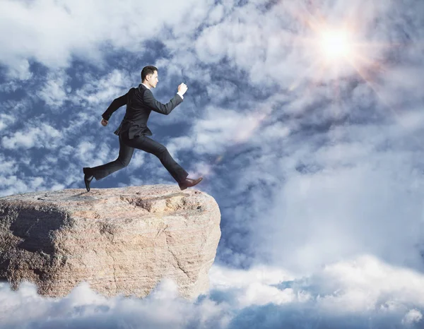 Vista lateral del joven hombre de negocios saltando desde el acantilado sobre el fondo del cielo. Concepto de riesgo — Foto de Stock