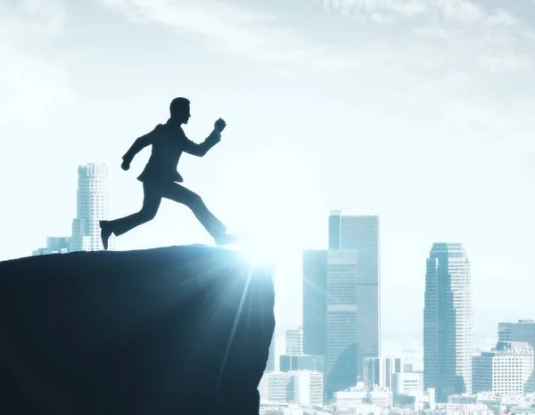 Backlit image of man silhouette jumping off cliff on city background. Achievement concept — Stock Photo, Image