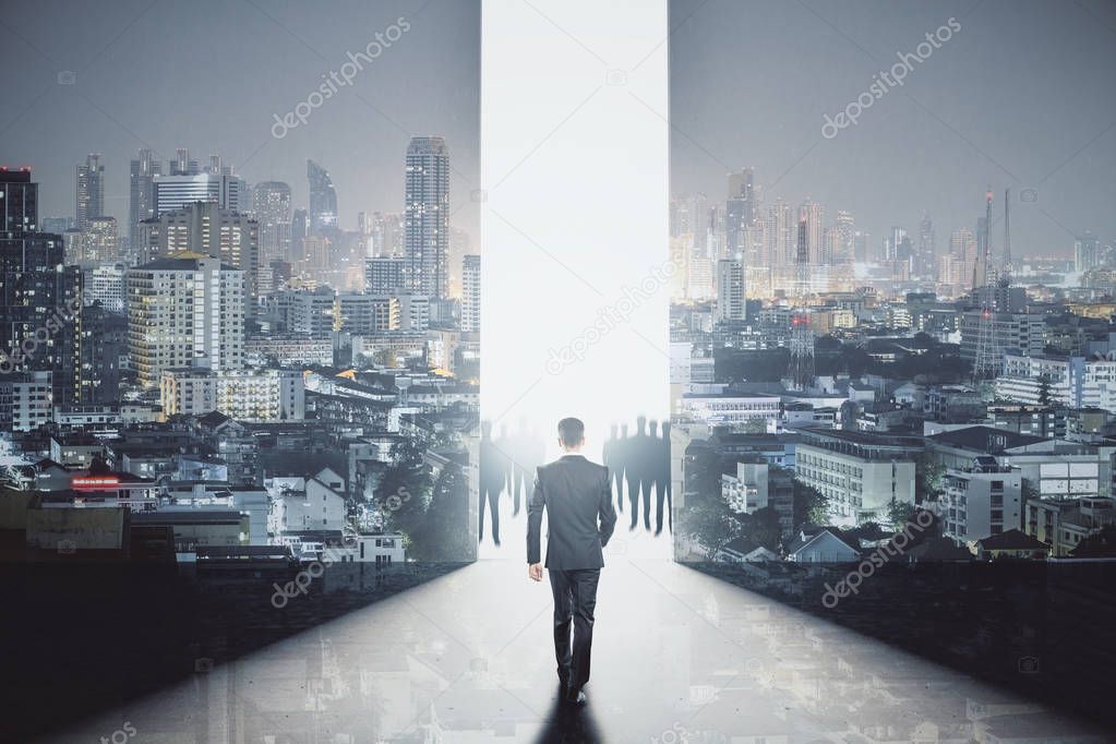 Back view of young businessman walking towards bright gap in abstract room interior with illuminated night city view. Bright future concept. Double exposure 