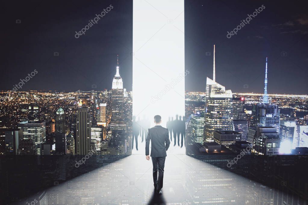Back view of young businessman walking towards bright gap in abstract room interior with illuminated night city view. Success concept. 