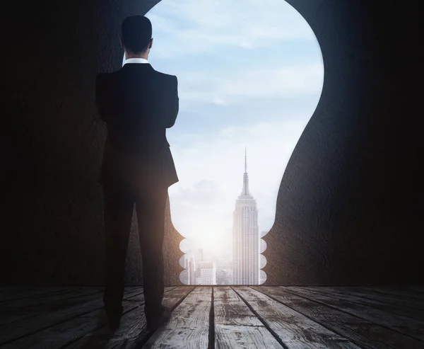 Back view of thoughtful young businessman standing in abstract room with light bulb opening, city view and daylight. Success concept. 3D Rendering — Stock Photo, Image