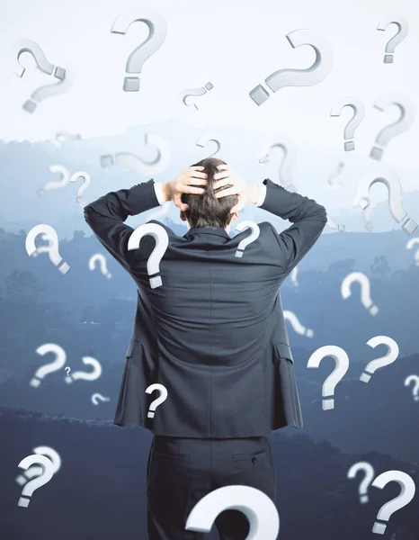 Back view of thinking young businessman on landscape background with question marks. Worried concept — Stock Photo, Image