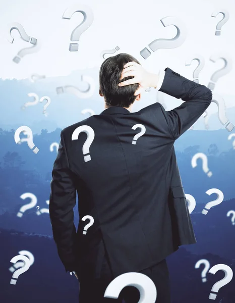 Back view of thinking young businessman on landscape background with question marks. Failure concept — Stock Photo, Image