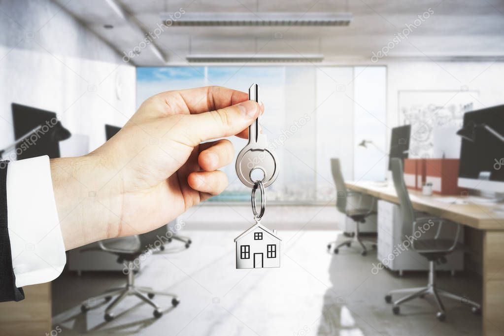 Businessman hand holding key with house keychain on blurry office interior background. Rent concept. 3D Rendering 