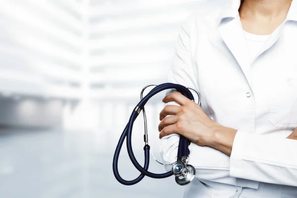 Oigenkännlig kvinnliga läkare med stetoskop och korslagda armar står på suddiga vit bakgrund med kopia utrymme. Medicin-konceptet — Stockfoto