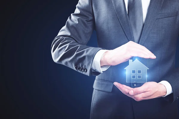 Businessman holding creative glowing house icon on blue background. Mortgage concept — Stock Photo, Image