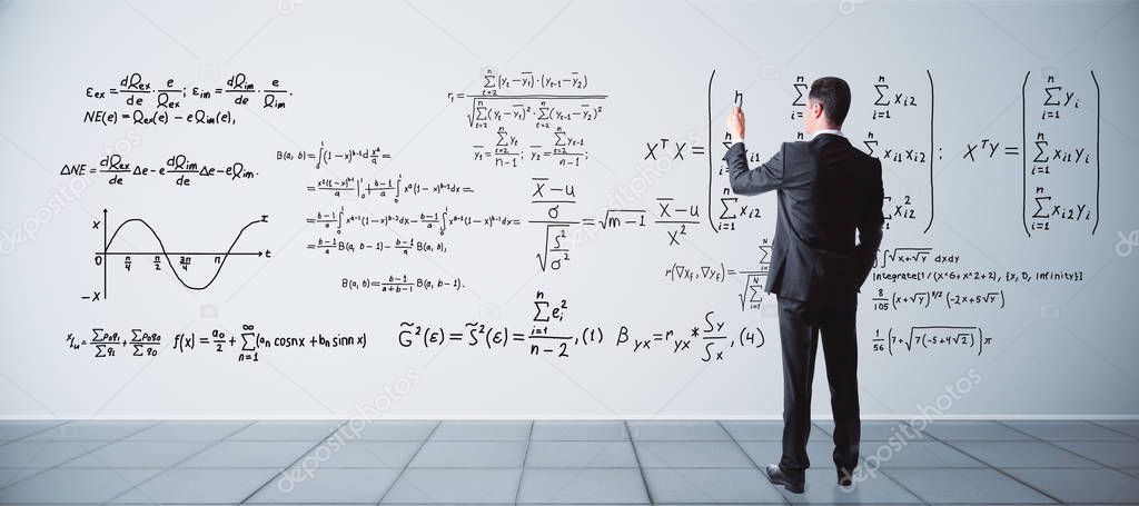 Back view of young businessman writing mathematical formulas on concrete wall in interior. Science concept