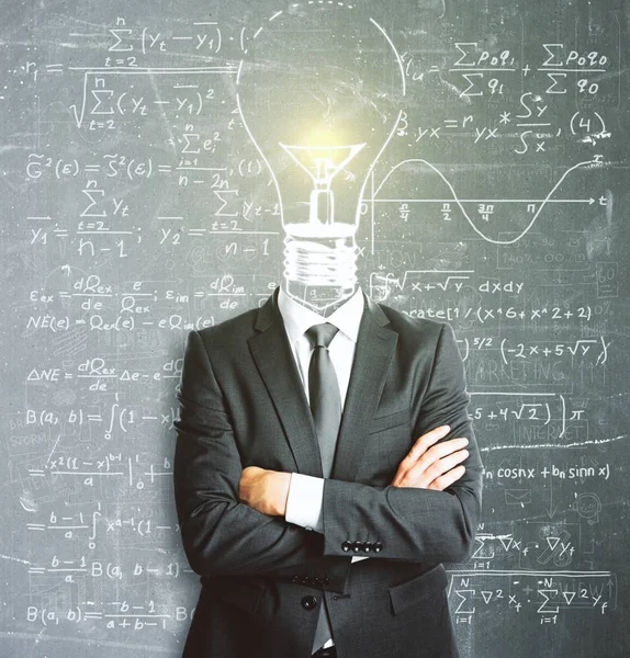 Light bulb headed businessman with folded arms standing on blackboard wall background with mathematical formulas. Problem concept — Stock Fotó