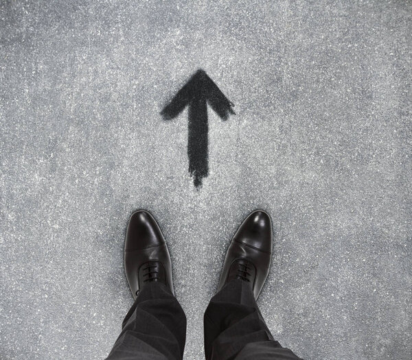 Top view of businessmen feet on concrete floor with drawn arrow. Motivation concept 