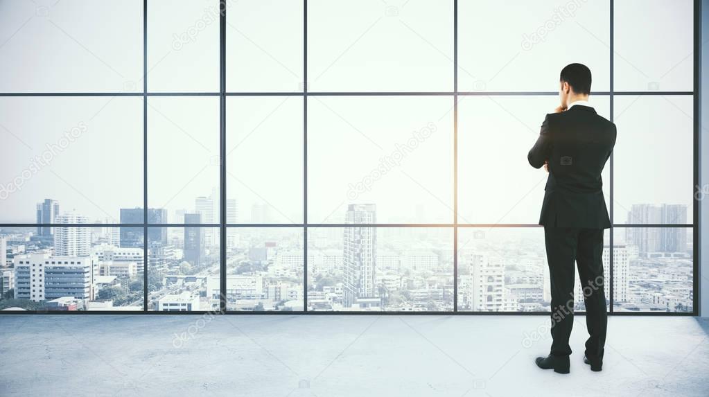 Back view of thoughtful young businessman standing in modern concrete office with panoramic city view and daylight. Think concept. 3D Rendering 