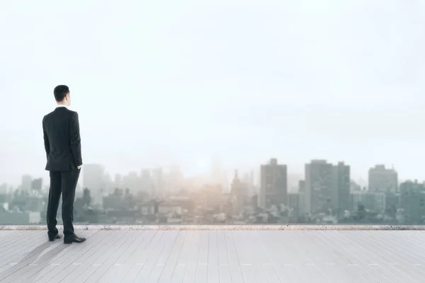 Back view of young businessman on rooftop looking into the distance on city background with sunlight — Stock Photo, Image