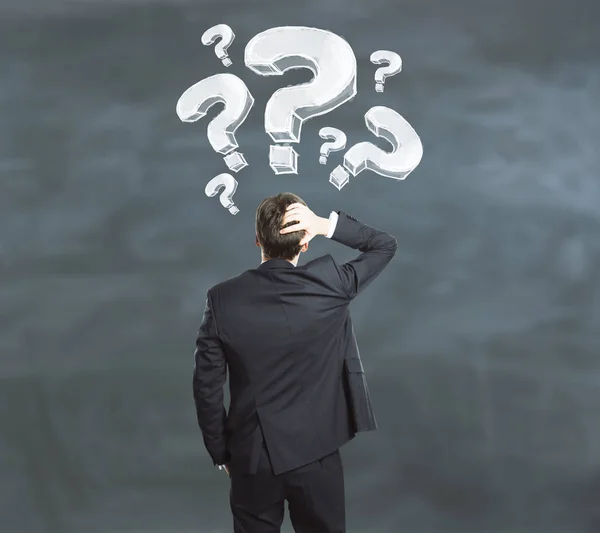 Businessman on chalkboard background looking at drawn question m — Stock Photo, Image