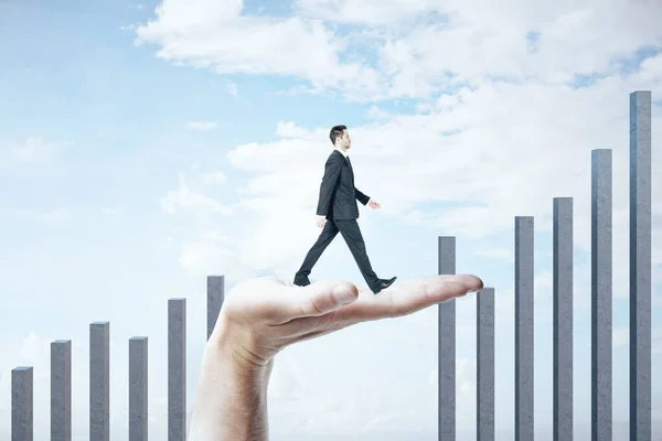 Hand helps a businessman climb on a business chart on a blue sky — 图库照片