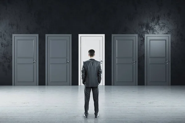 Businessman standing in gray room and looking on five closed doors. Business and challenge concept.
