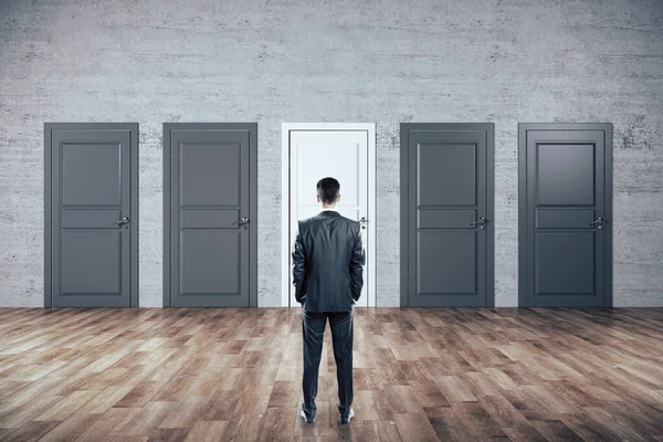 Businessman standing in room and looking on five closed doors. Business and motivation concept.
