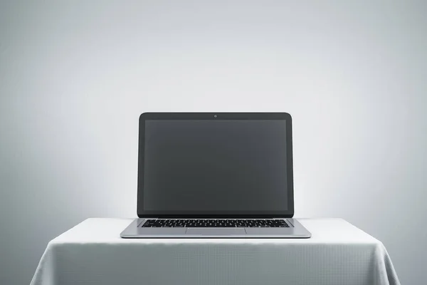 Creative designer desktop with empty black laptop computer screen on gray wall background. Mock up. 3D Rendering