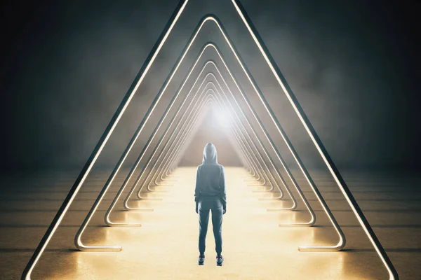 Hacker standing in interior with abstract luminous triangle corridor. Innovation and modern concept.