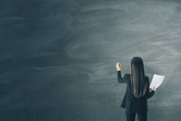 Businesswoman with document in hand drawing on blank blackboard. Business and success concept.