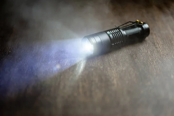 Тактичний водонепроникний ліхтарик. Світлодіодний ліхтарик світить на столі в диму . — стокове фото