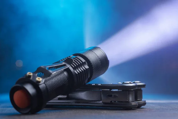 Tactical waterproof flashlight. LED flashlight shines on the table in smoke.