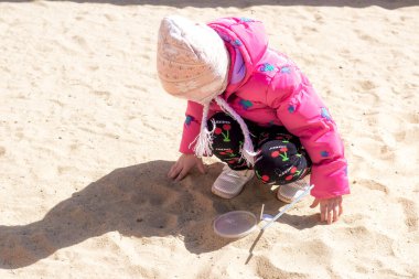 Pembe ceketli çocuk kumlarda oynuyor.