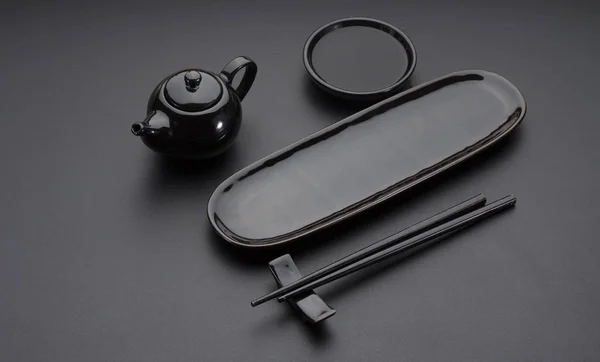 Schwarzes klares Geschirr für Sushi und Brötchen. Japanische Essstäbchen, Teller, Untertasse auf dem schwarzen Tisch. — Stockfoto