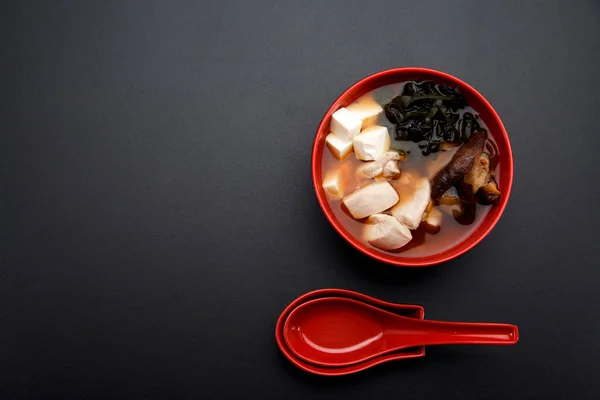 Sopa de miso japonesa en un tazón rojo y cuchara en la mesa . — Foto de Stock