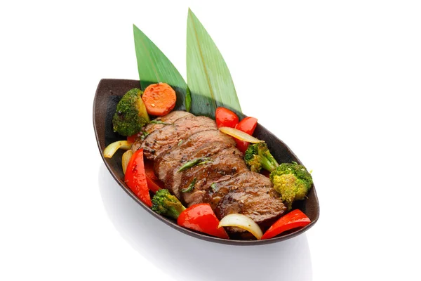 Жареная телятина с овощами на черной тарелке изолированы на белом фоне — стоковое фото