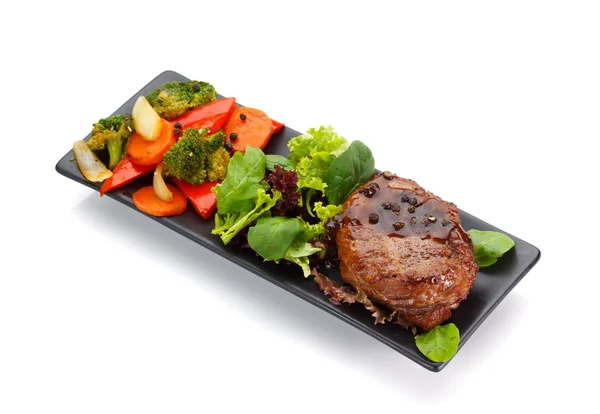 Kalvkött steake med grönsaker på en svart plåt isolerad på vit bakgrund — Stockfoto