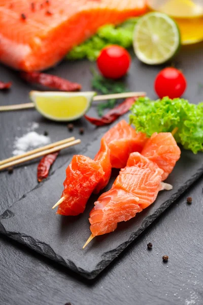 Rauwe zalm spiesjes op een stenen plaat. tomaten, kalk en sla voor het koken. — Stockfoto