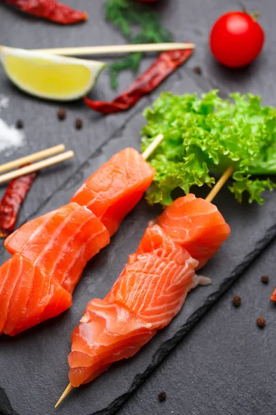 Raw salmon skewers on a stone plate. tomatoes, lime and lettuce for cooking. — Stock Photo, Image