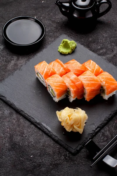 Japanese cuisine. Salmon sushi roll (philadelphia) on a stone plate and dark concrete background.
