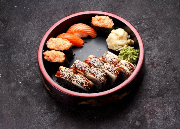 Cozinha japonesa. Rolo de sushi definido em uma placa de madeira redonda e fundo de concreto escuro . — Fotografia de Stock