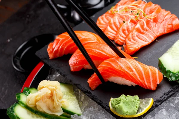 Japanese cuisine. Salmon sushi and sashimi on a stone plate and ice and dark concrete background. — Stock Photo, Image