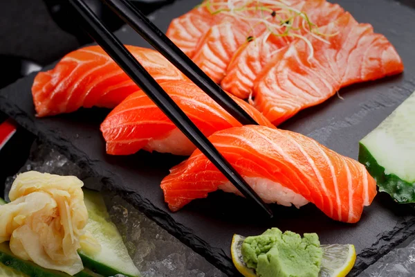 Japanese cuisine. Salmon sushi and sashimi on a stone plate and ice and dark concrete background. — Stock Photo, Image